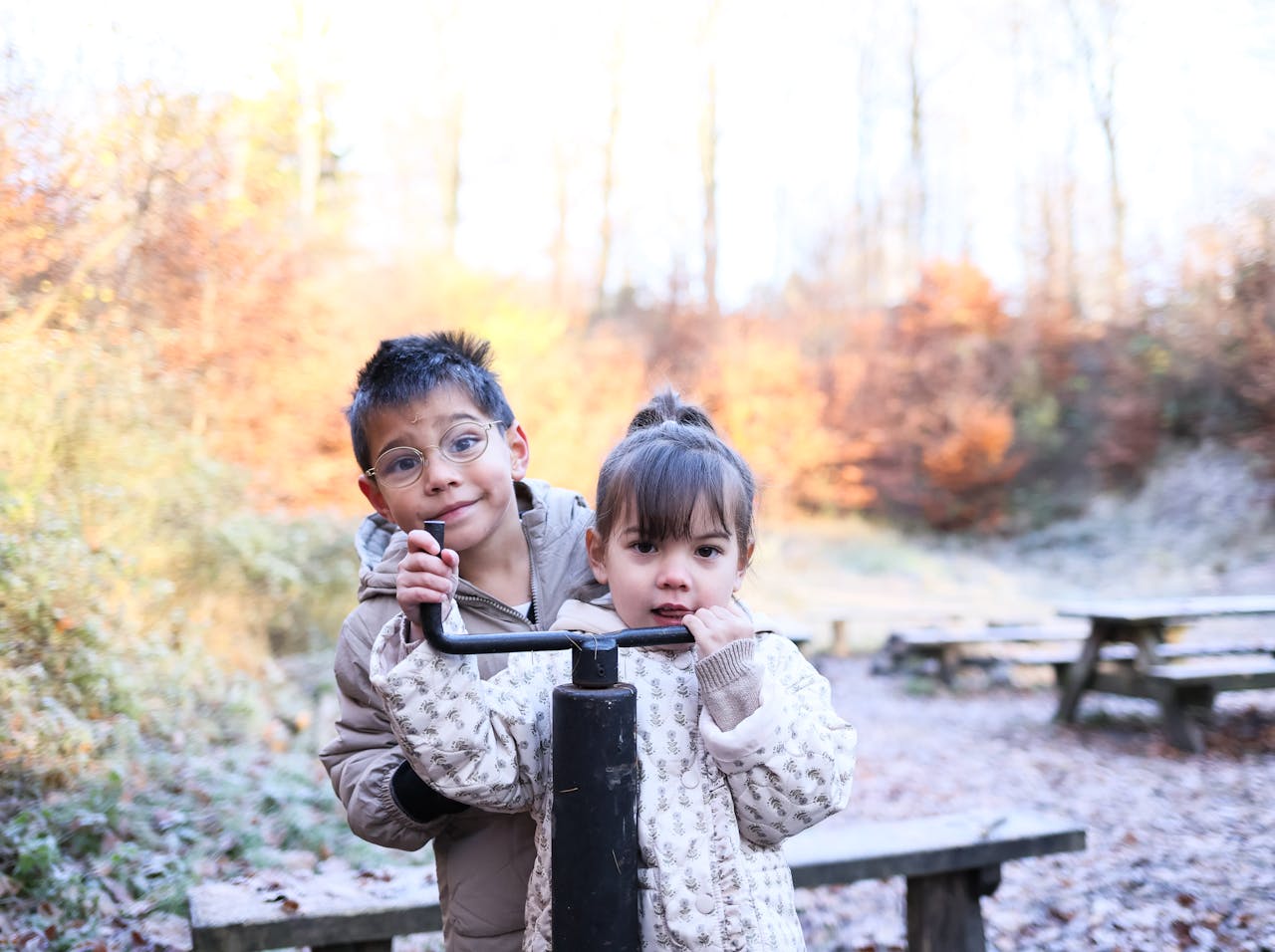 services-01 Two kids playing with a water pump at a park in autumn, surrounded by colorful fall foliage.