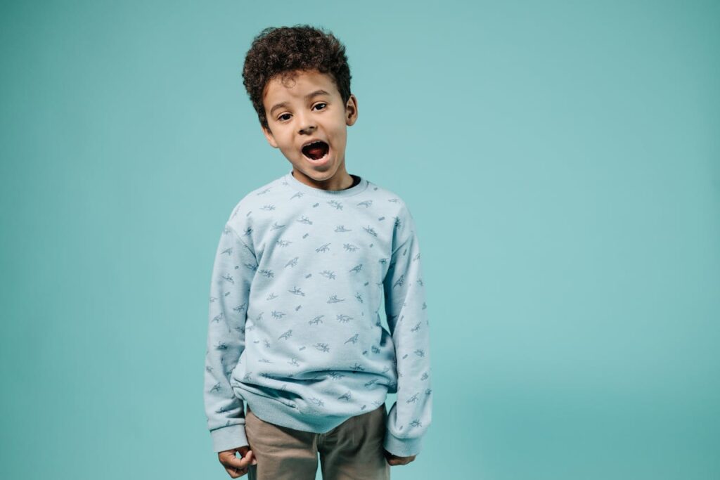 Cheerful child in a blue sweater smiling against a turquoise backdrop.